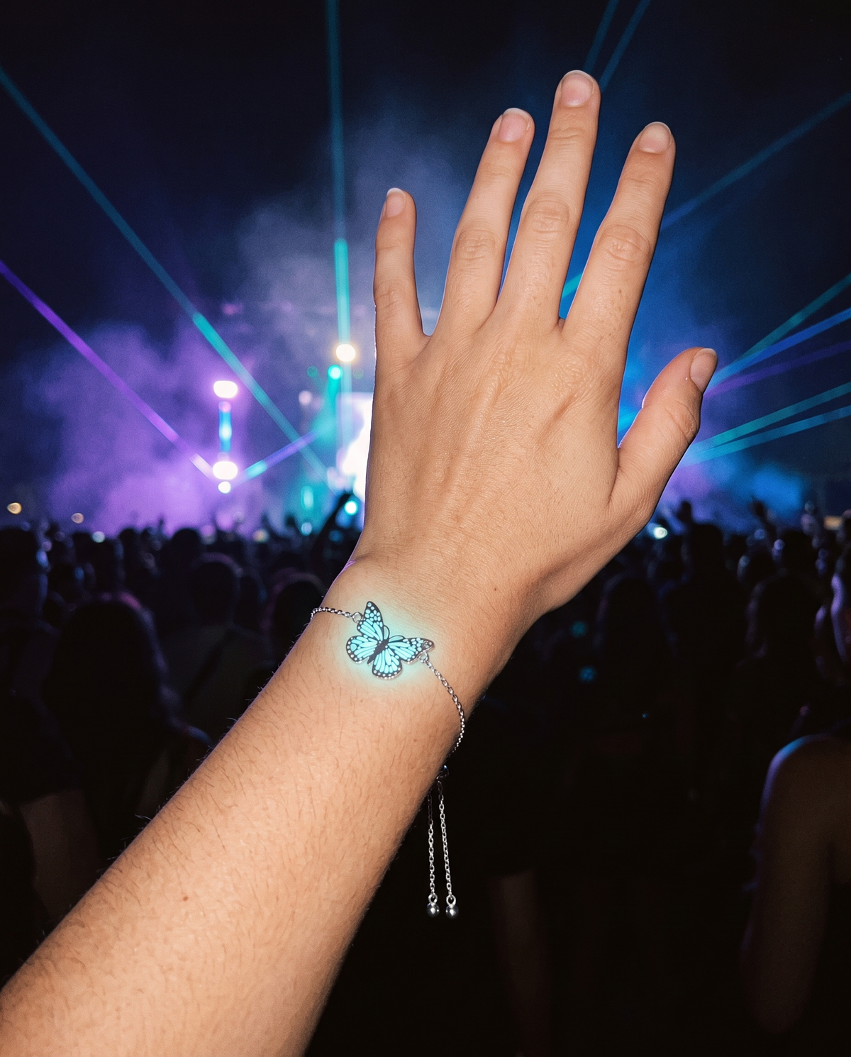 Hand raised at a night festival wearing the Giant Butterfly bracelet glowing cyan