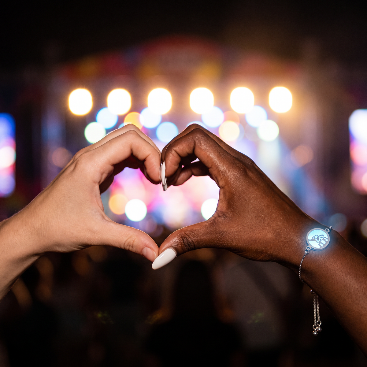 Luminous Baby Elephant Bracelet worn at night. Friends making a heart at the main stage.