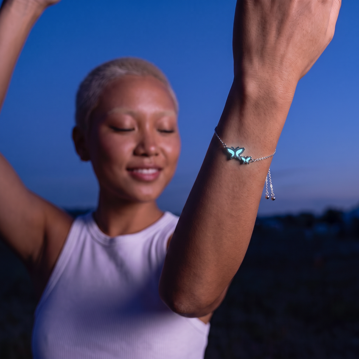 Luminous Twin Butterfly Bracelet worn at night. Blue hour, arms up.